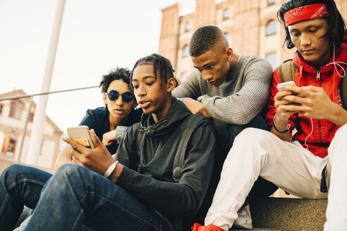 Männliche Freunde benutzen Mobiltelefone, während sie in der Stadt sitzen - MASF11805