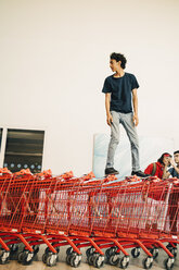 Unbekümmerter Teenager, der auf gestapelten roten Einkaufswagen vor einem Einkaufszentrum steht - MASF11815