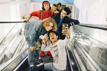 Glückliche männliche Freunde, die ein Selfie mit einem Smartphone auf einem Laufsteg in einem Einkaufszentrum machen - MASF11823