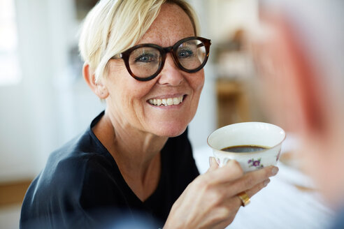 Smiling mature woman holding coffee cup while looking away at home - MASF11829