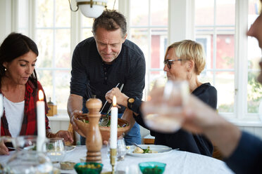 Mature man serving food to female friends at home - MASF11835