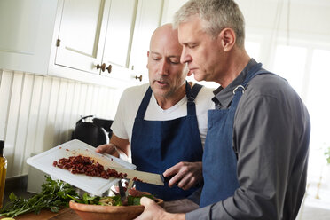 Bald mature man assisting friend in cooking food at home - MASF11841
