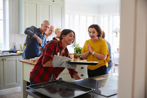 Excited woman looking at friend baking in kitchen at home stock photo