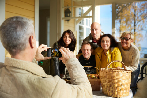 Mature man photographing friends with smart phone on porch stock photo