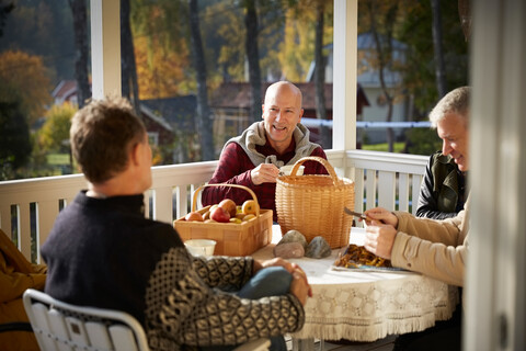 Glückliche reife Männer unterhalten sich auf der Veranda sitzend, lizenzfreies Stockfoto