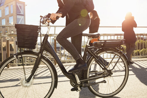 Niedriger Ausschnitt einer reifen Frau, die auf einer Brücke in der Stadt gegen den Himmel mit einem Elektrofahrrad fährt - MASF11865