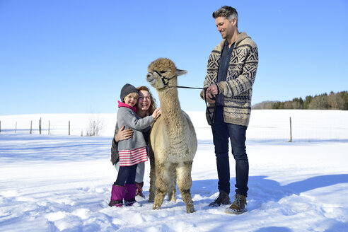 Glückliche Familie mit Alpaka auf einer Wiese im Winter - ECPF00565