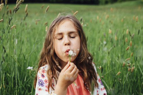 Porträt eines Mädchens, das eine Pusteblume auf einer Wiese bläst - ANHF00099
