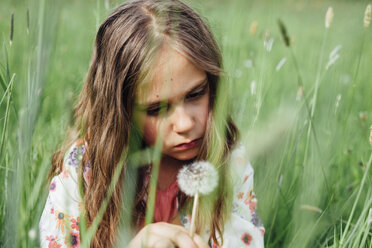 Porträt eines unglücklichen Mädchens, das eine Pusteblume auf einer Wiese betrachtet - ANHF00100