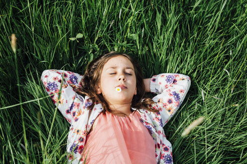 Porträt eines Mädchens, das sich auf einer Wiese mit einem Gänseblümchen im Mund entspannt - ANHF00101