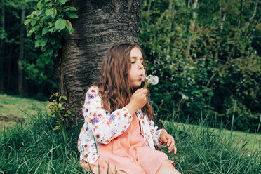 Portrait of girl sitting on a meadow blowing blowball - ANHF00103