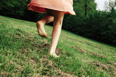 Rückenansicht eines barfuß laufenden Mädchens auf einer Wiese, Teilansicht - ANHF00104