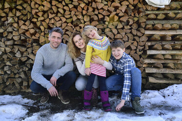 Porträt einer glücklichen Familie vor einem Holzstapel im Winter - ECPF00597