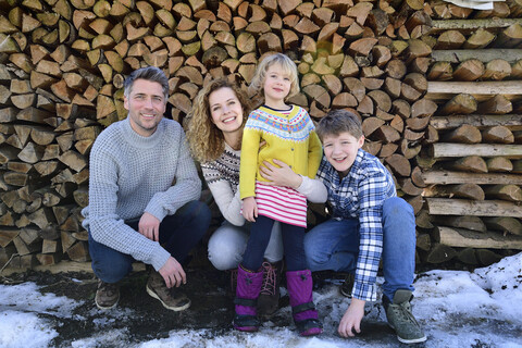 Porträt einer glücklichen Familie vor einem Holzstapel im Winter, lizenzfreies Stockfoto