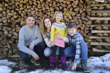 Porträt einer glücklichen Familie vor einem Holzstapel im Winter - ECPF00598