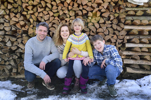 Porträt einer glücklichen Familie vor einem Holzstapel im Winter - ECPF00599