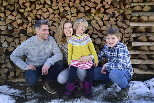 Porträt einer glücklichen Familie vor einem Holzstapel im Winter - ECPF00600