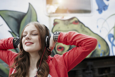 Portrait of teenage girl wearing headphones at a painted train car - RORF01815