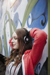 Portrait of teenage girl wearing headphones at a painted train car - RORF01816