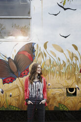 Lächelndes Teenager-Mädchen, das an einem bemalten Eisenbahnwagen steht - RORF01820