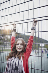 Portrait of a happy teenage girl at a fence at a sports field - RORF01825