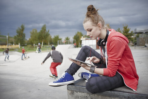 Teenage girl using a tablet at a skatepark - RORF01837
