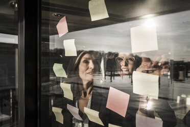 Zwei Geschäftsfrauen beim Brainstorming, Klebezettel an der Fensterscheibe - MJRF00083