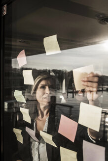 Two businesswomen brainstorming, putting sticky notes on window pane - MJRF00089