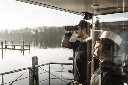 Colleagues working on a houseboat, watching surroundings with binoculars - MJRF00099