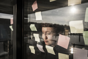 Tired woman leaning against window pane with sticky notes - MJRF00107