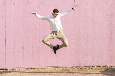 Exuberant young man jumping in front of pink wall - UUF16748