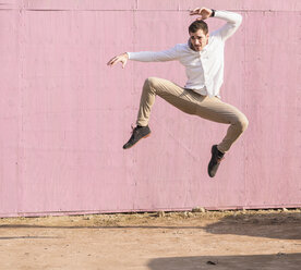 Exuberant young man jumping in front of pink wall - UUF16750
