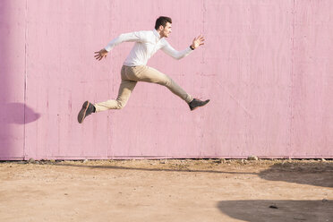 Exuberant young man jumping in front of pink wall - UUF16751
