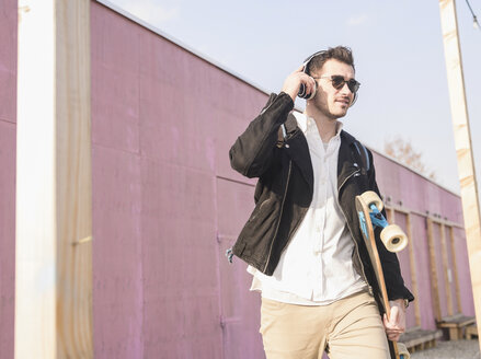 Young man with skatebaord and headphones on the move in the city - UUF16757