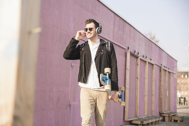 Young man with skatebaord and headphones on the move in the city - UUF16758