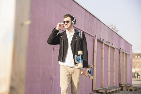 Junger Mann mit Skateboard und Kopfhörern unterwegs in der Stadt - UUF16758
