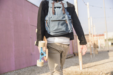 Rückansicht eines jungen Mannes mit Skateboard und Rucksack, der in der Stadt unterwegs ist - UUF16759