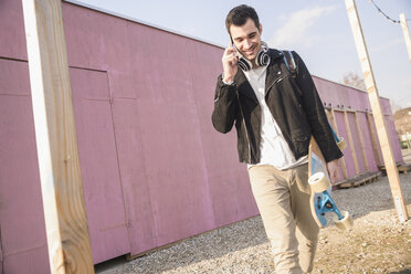 Junger Mann mit Skateboard und Mobiltelefon unterwegs - UUF16760