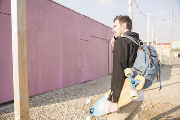 Junger Mann mit Skateboard und Mobiltelefon in der Stadt unterwegs - UUF16761