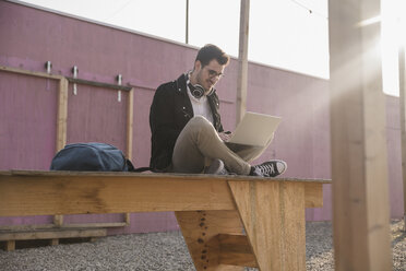 Junger Mann sitzt auf einem Bahnsteig und benutzt einen Laptop - UUF16764