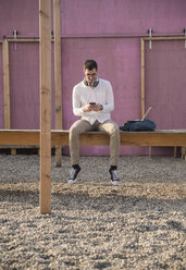 Young man sitting on platform using cell phone - UUF16766