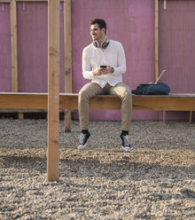 Young man sitting on platform holding cell phone - UUF16767