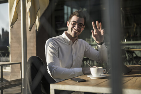 Lächelnder junger Mann mit Tablet in einem Straßencafé winkt, lizenzfreies Stockfoto