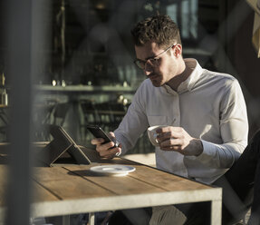 Junger Mann benutzt Handy und Tablet in einem Straßencafé - UUF16786