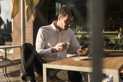 Junger Mann benutzt Handy und Tablet in einem Straßencafé, lizenzfreies Stockfoto