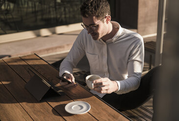 Junger Mann benutzt Handy und Tablet in einem Straßencafé - UUF16788