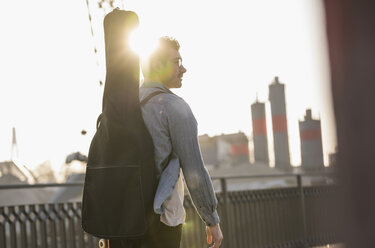 Junger Mann mit Gitarrenkoffer in der Stadt bei Sonnenuntergang - UUF16789