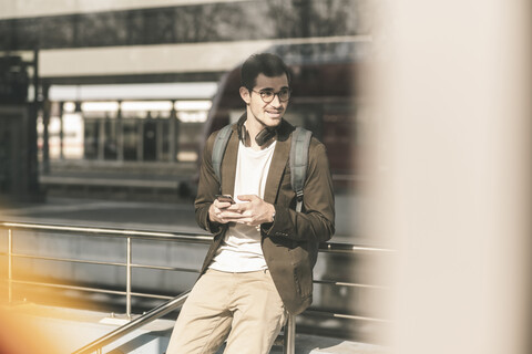 Lächelnder junger Mann mit Mobiltelefon am Bahnhof, lizenzfreies Stockfoto