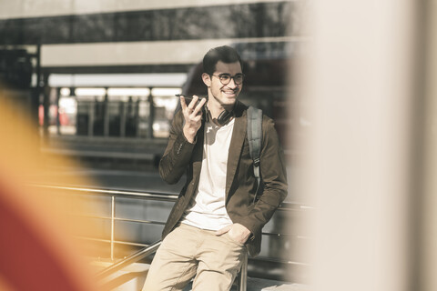 Lächelnder junger Mann, der am Bahnhof ein Mobiltelefon benutzt, lizenzfreies Stockfoto
