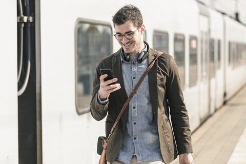 Lächelnder junger Mann mit Mobiltelefon am Bahnsteig, lizenzfreies Stockfoto